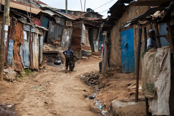 The image reveals clustered rusty homes on untarred road. 
